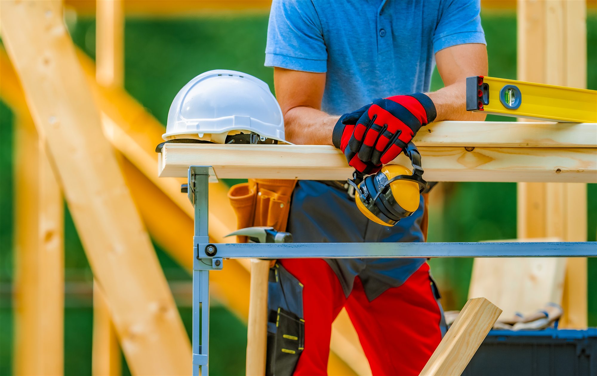 Construction worker holding hearing protection beside tools and timber framing