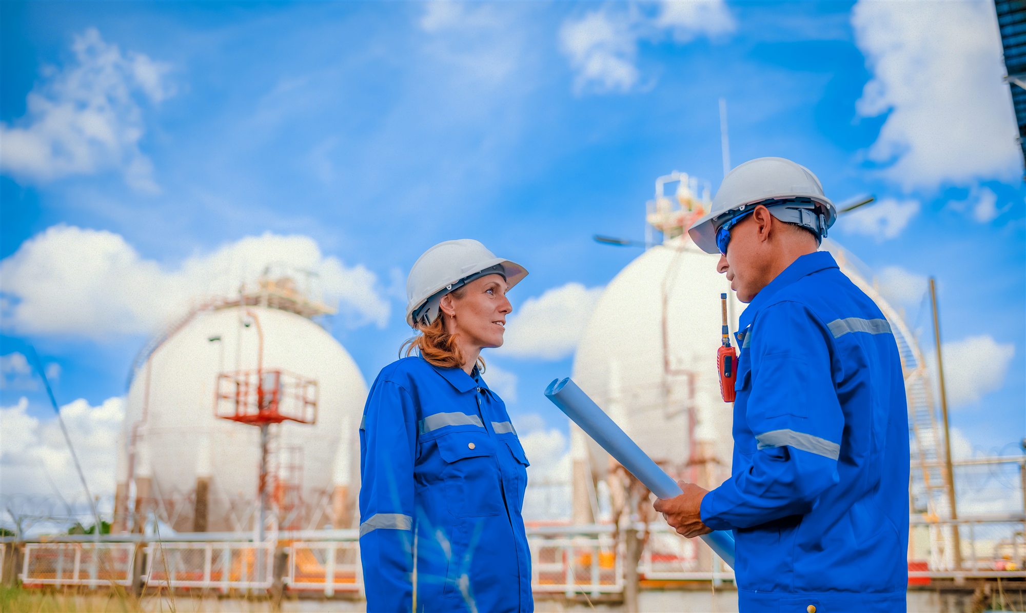 Two engineers discussing plans in front of industrial storage vessels