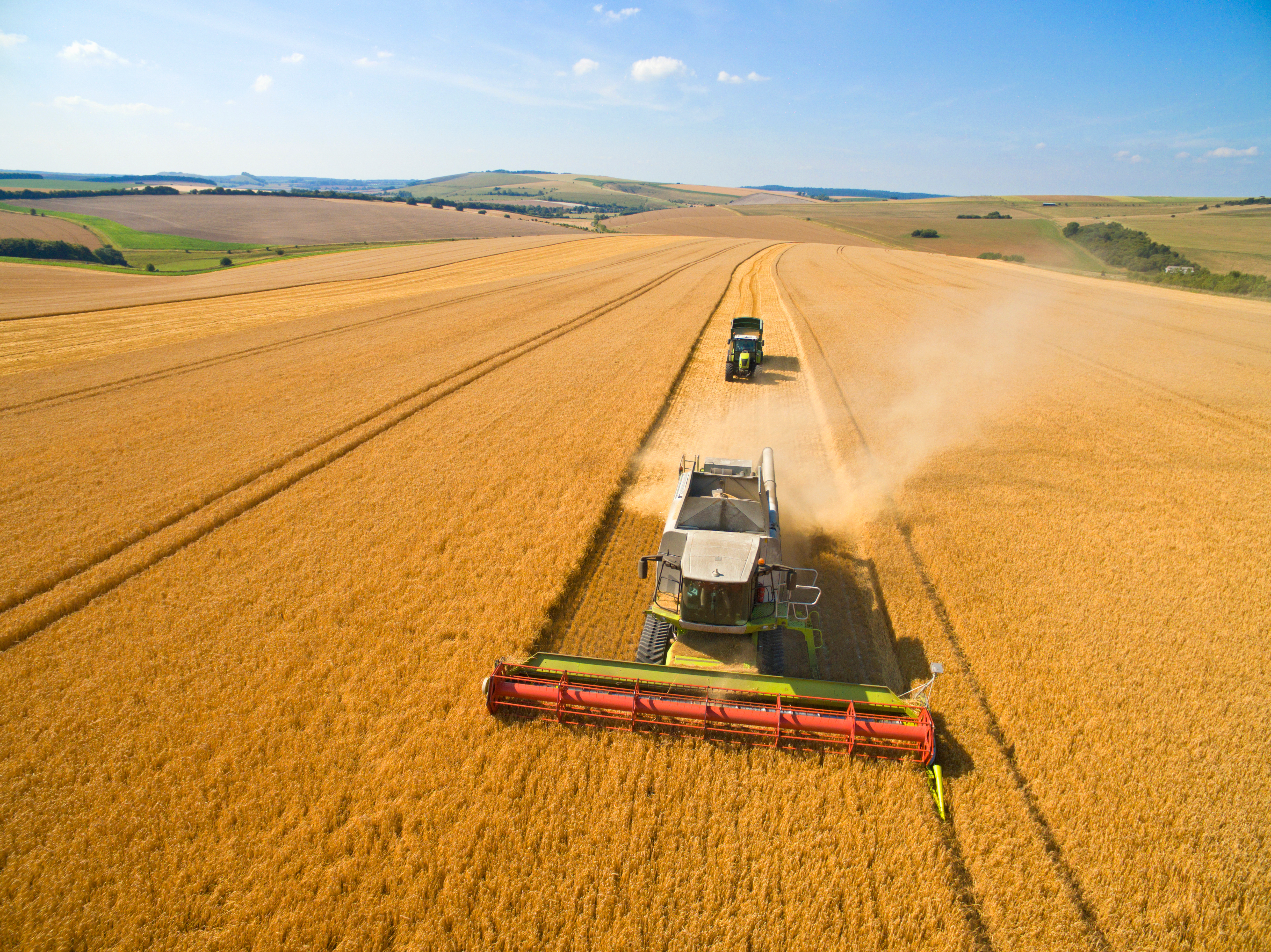 Wide aerial harvest scene with combine and tractor moving through grain fields
