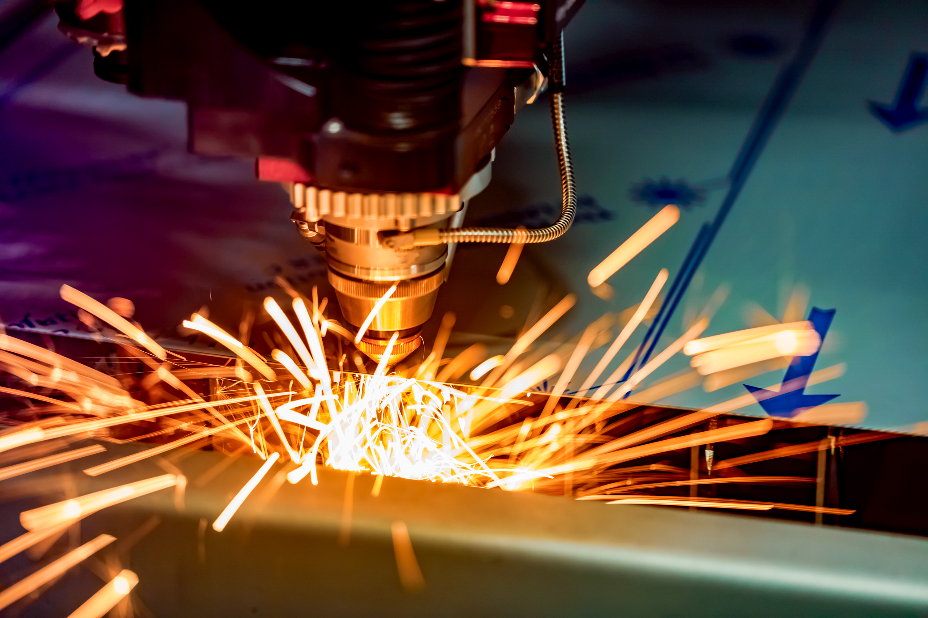 Close view of an industrial laser cutting metal with bright safety-orange sparks
